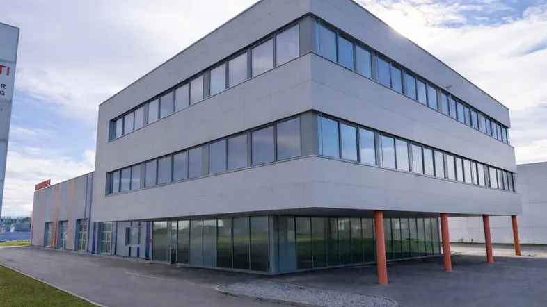 Modernes Geschäftsgebäude mit heller Fassade und großen Fenstern. Die Architektur zeichnet sich durch klare Linien und orangefarbene Stützen aus.
