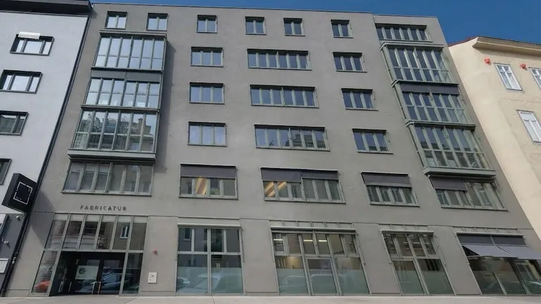 Modernes Gebäude mit grauer Fassade, großen Fenstern und integrierten Loggien in städtischer Umgebung.