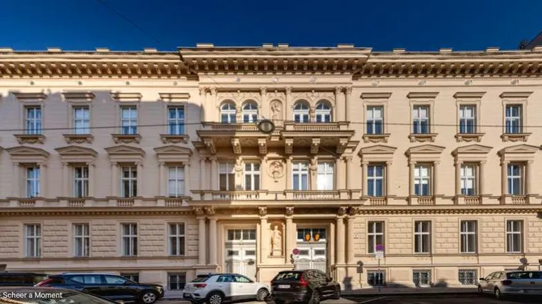 Prächtige historische Fassade eines Altbaus mit vielen Fenstern und dekorativen Elementen, direkt an einer Straße gelegen.