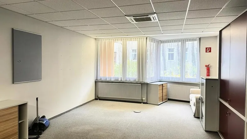 Geräumiges Büro mit Teppichboden, großen Fenstern und abgehängter Decke, bereit zur Einrichtung.