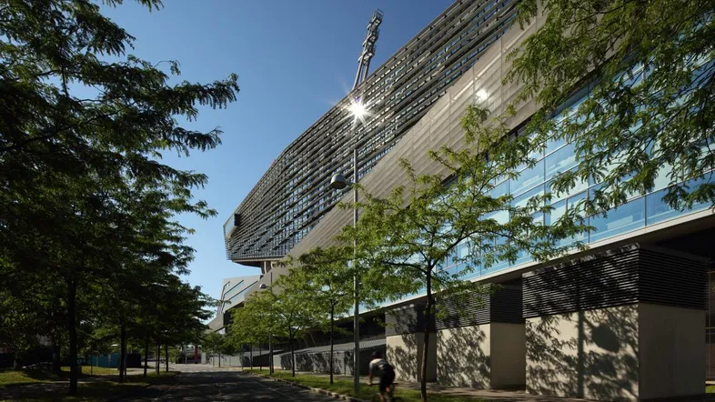 Moderne Architektur eines großen Gebäudes mit Glasfassade und Bäumen entlang der Straße unter blauem Himmel.
