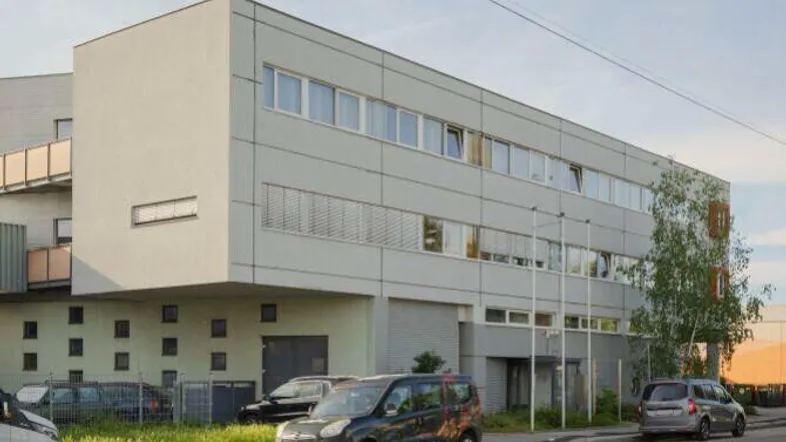 Modernes Bürogebäude mit heller Fassade und großen Fenstern an einer Straße mit parkenden Autos.