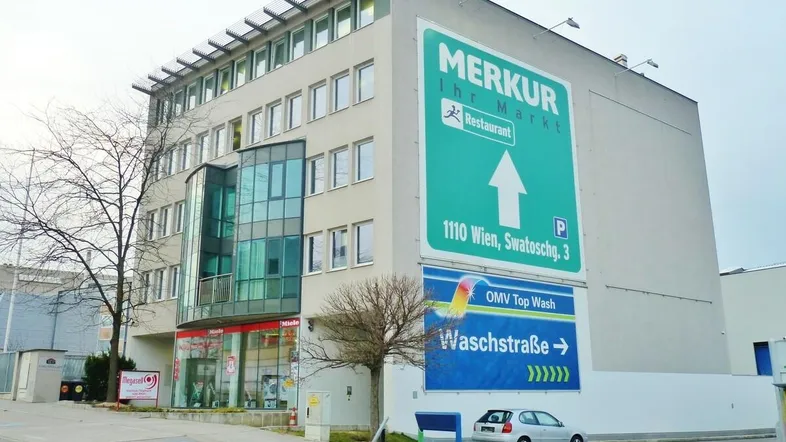 Mehrstöckiges Geschäftsgebäude mit großen Werbetafeln, moderner Glasfassade und einem geparkten Auto davor.