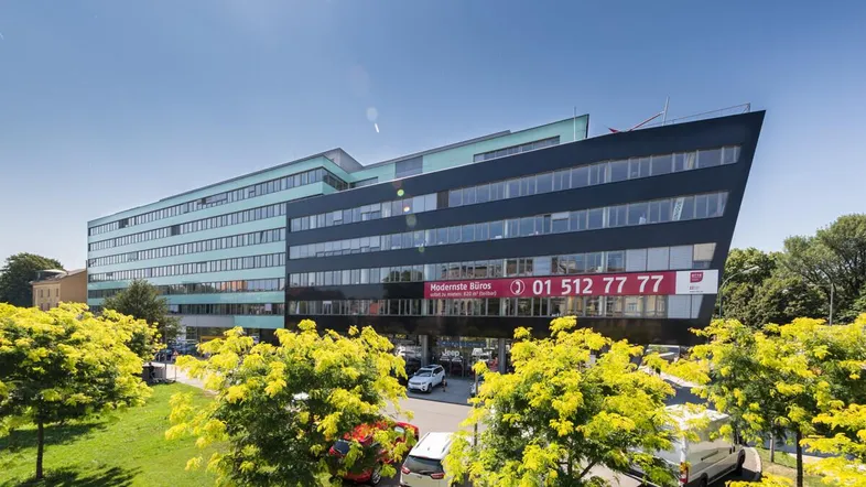 Modernes Bürogebäude mit markanter schwarzer und hellblauer Fassade, umgeben von Grünflächen und Parkplätzen.