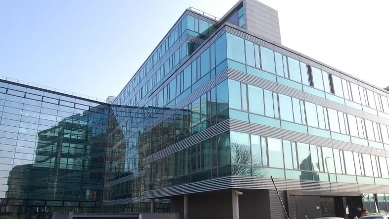 Modernes Bürogebäude mit auffälliger Glasfassade und reflektierenden Fenstern unter klarem Himmel.