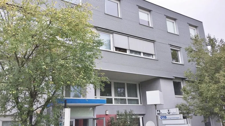Modernes Geschäftsgebäude mit geriffelter Fassade und großen Fenstern, umgeben von Bäumen.