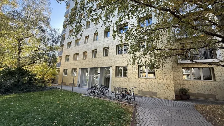 Fassade eines modernen Mehrfamilienhauses mit Grünflächen und Fahrradstellplätzen im Herbstlicht.
