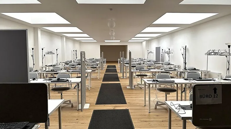 Großer, heller Büroraum mit vielen Arbeitsplätzen, Holzfußboden und modernen Deckenleuchten.