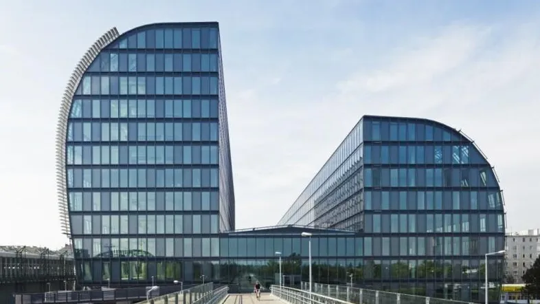 Modernes Bürogebäude mit geschwungener Glasfassade und einer Fußgängerbrücke, die zum Eingang führt.