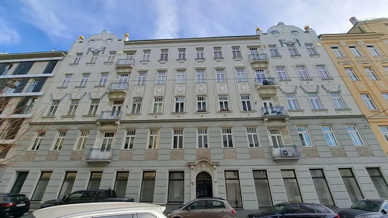 Historisches Gebäude mit klassischer Fassade und vielen Fenstern, umgeben von parkenden Autos auf der Straße.