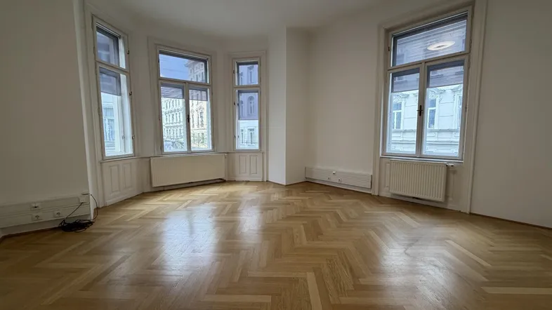 Geräumiger Büroraum mit Fischgrätparkett und großen Fenstern, die viel Tageslicht hereinlassen.