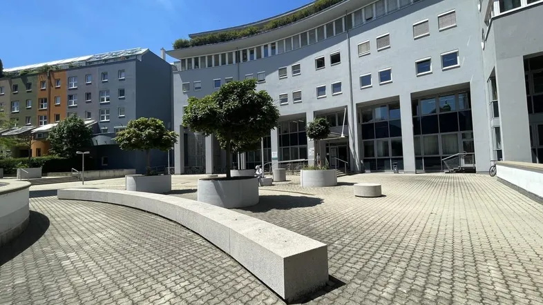 Moderner Gebäudekomplex mit geschwungener Fassade und einem gepflasterten Innenhof unter blauem Himmel.