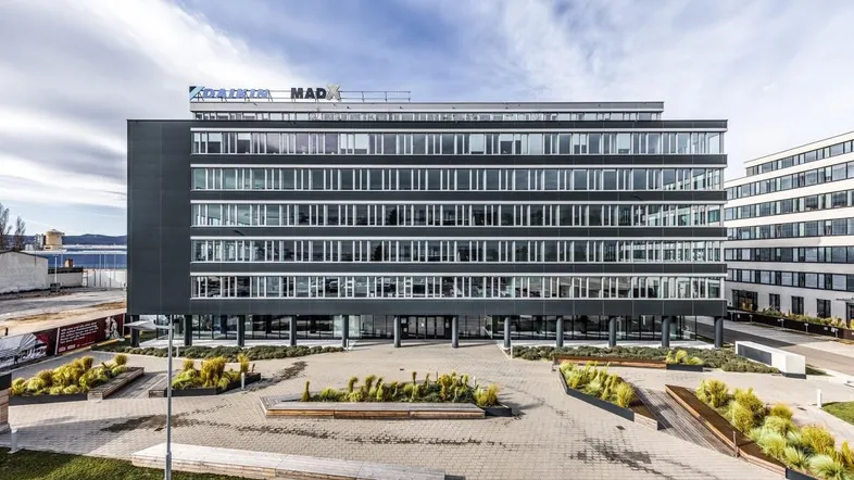 Modernes Bürogebäude mit großer Glasfassade und gepflegter Außenanlage unter bewölktem Himmel.