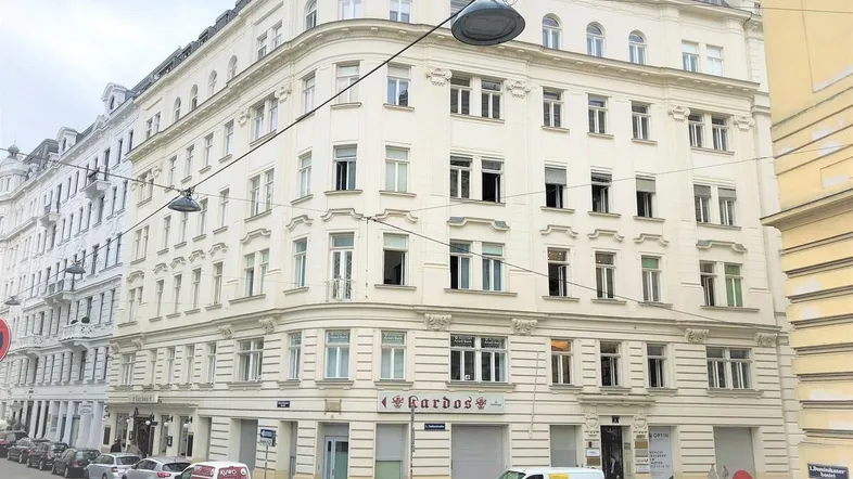 Historisches Eckgebäude mit klassischer Architektur und vielen Fenstern an einer belebten Straße.