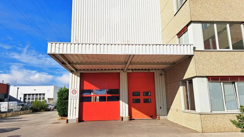 Industrielles Gebäude mit zwei großen roten Rolltoren und einer Überdachung, davor ein asphaltierter Bereich.
