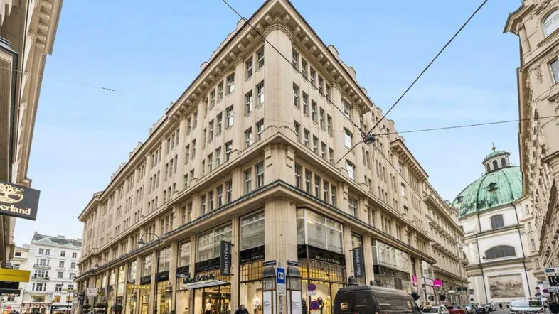 Historisches Eckgebäude mit vielen Fenstern und Geschäften im Erdgeschoss in einer belebten Stadtstraße.