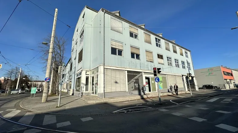 Außenansicht eines Geschäftsgebäudes an einer Straßenecke mit Straßenbahnschienen und blauer Fassade.