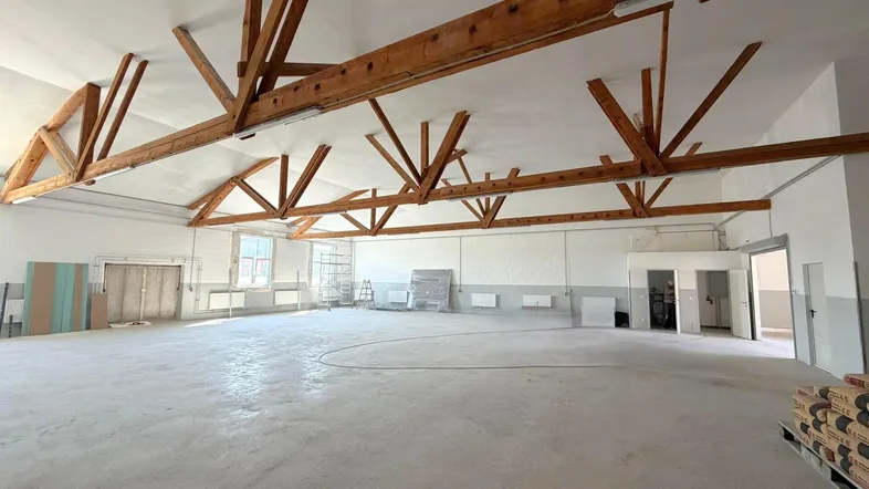 Großer, leerer Raum mit sichtbaren Holzsparren an der Decke und Betonboden, ideal für Lager oder Produktion.