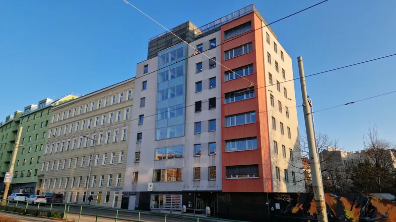 Modernes Gebäude mit gemischter Fassade und großen Fenstern an einer Straße mit Straßenbahnschienen.