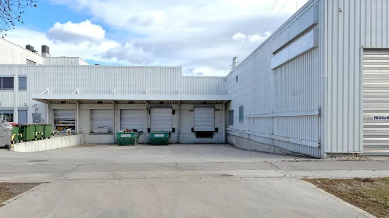 Außenansicht eines Industriegebäudes mit mehreren Laderampen und einem großen Vorplatz unter bewölktem Himmel.