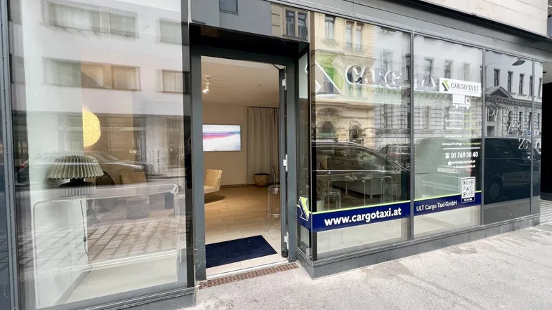 Moderne Geschäftsfassade mit großen Glasfenstern und offener Eingangstür, die einen Blick ins Innere gewährt.