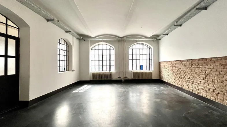 Geräumiger, leerer Raum mit hohen Decken, großen Bogenfenstern und einer Akzentwand aus Ziegeln.