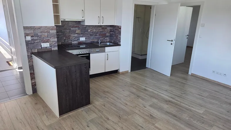 Moderne offene Küche mit weißen Schränken, dunkler Arbeitsplatte und Laminatboden in offenem Wohnbereich.