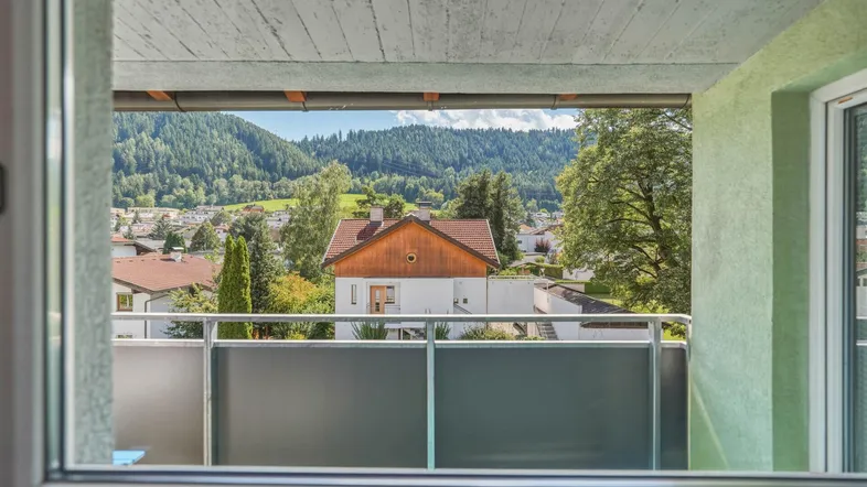 Blick aus einem Innenraum auf einen Balkon mit Bergblick und umliegende Häuser.
