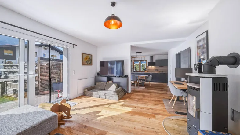 Helles Wohnzimmer mit Holzboden, Kaminofen und Zugang zur Terrasse, offen zum Essbereich und Küche.