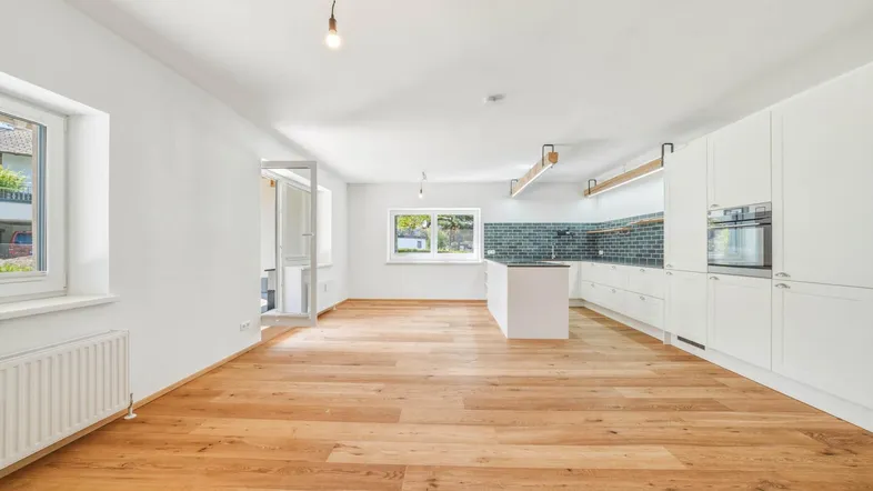 Heller offener Wohnbereich mit moderner Einbauküche, Holzboden und Zugang zum Außenbereich.