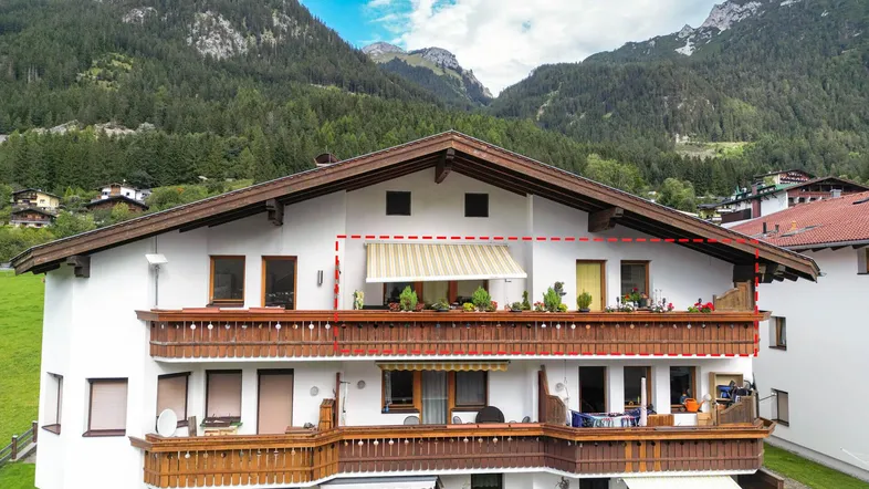 Traditionelles Mehrfamilienhaus mit mehreren Holzbalconen und Bergblick in alpiner Umgebung.