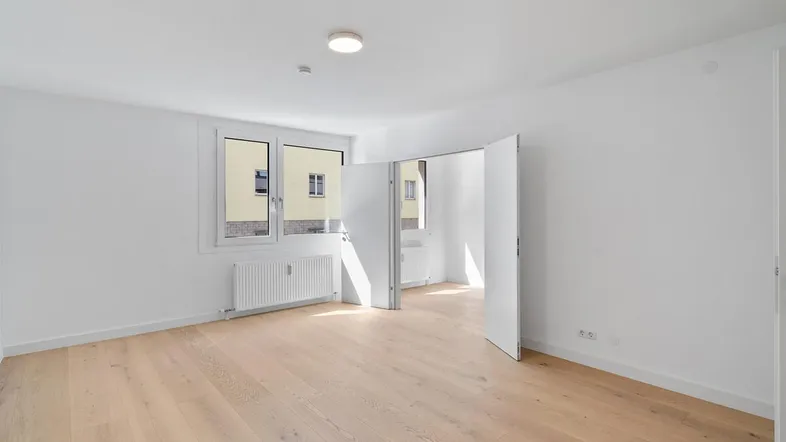 Helles, leeres Zimmer mit Holzparkettboden und großen Fenstern, bereit zur individuellen Gestaltung.