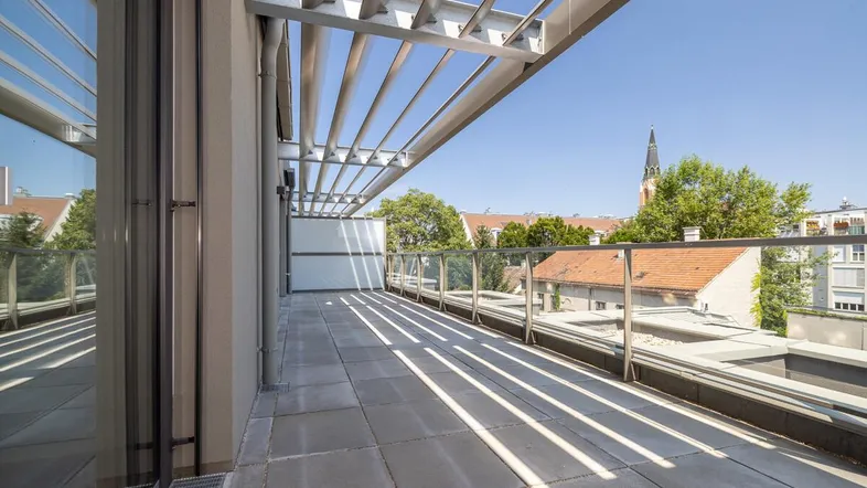 Große, sonnige Terrasse mit modernen Fliesen, Glasgeländer und Blick auf die Stadt.