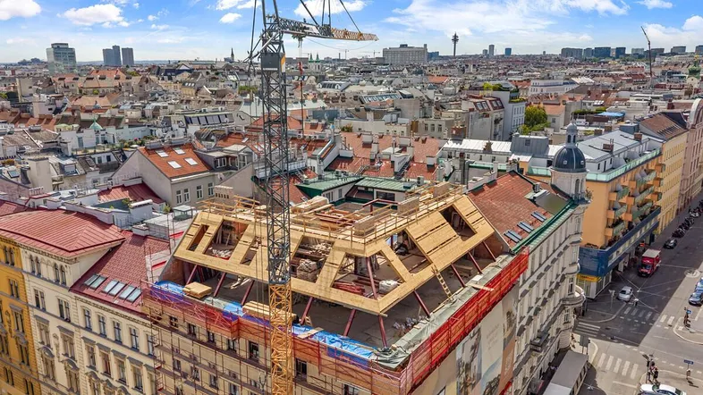 Luftaufnahme eines Gebäudes im Bau mit Kran und Dachstuhl in einer städtischen Umgebung.