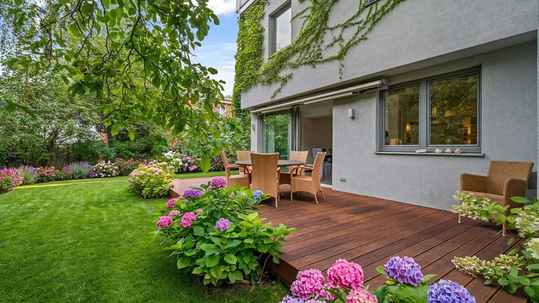 Große Holzterrasse mit Gartenmöbeln, umgeben von einem gepflegten Rasen und blühenden Hortensien.