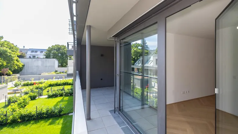 Geräumiger Balkon mit Fliesenboden und Blick auf den gepflegten Gemeinschaftsgarten.