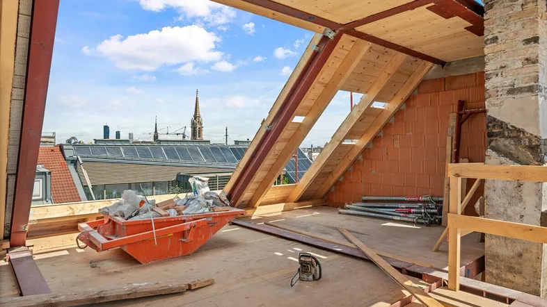 Unfertiger Dachboden mit Holzbalken und Blick auf die Stadt, bereit für den Ausbau.
