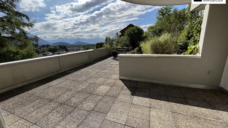 Geräumige Sonnenterrasse mit Fliesenboden und weitem Blick auf die umliegende Berglandschaft und die Stadt.