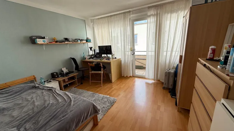 Helles Schlafzimmer mit Holzboden, Schreibtisch und direktem Zugang zu einem kleinen Balkon.