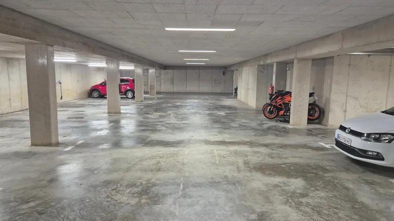Geräumige Tiefgarage mit Betonwänden und -boden, bietet Platz für mehrere Fahrzeuge und Motorräder.