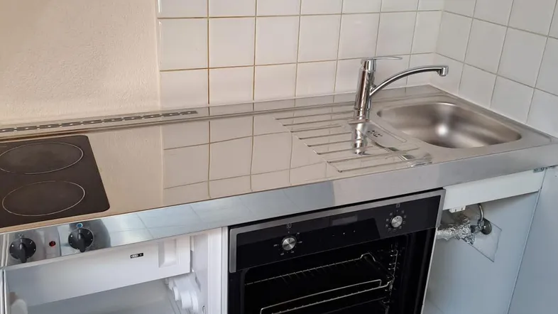 Kleine Küchenzeile mit integriertem Backofen, Kochfeld und Kühlschrank, ideal für kompakte Wohnräume.