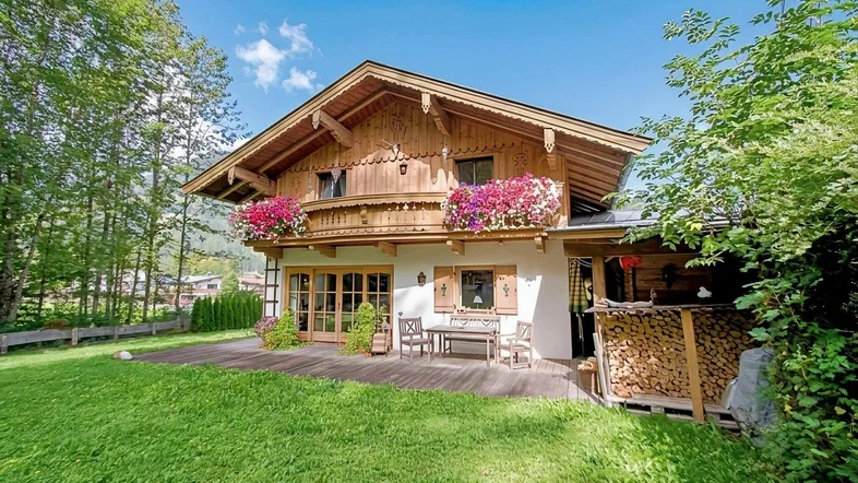 Traditionelles Chalet mit Holzbalkonen, blühenden Blumenkästen und großer Rasenfläche.