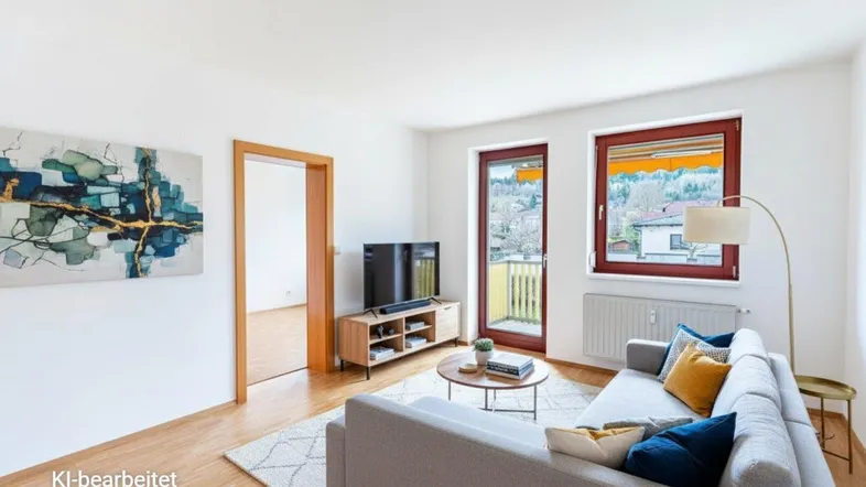 Helles Wohnzimmer mit bequemer Couch, Fernseher und Zugang zum Balkon mit schöner Aussicht.