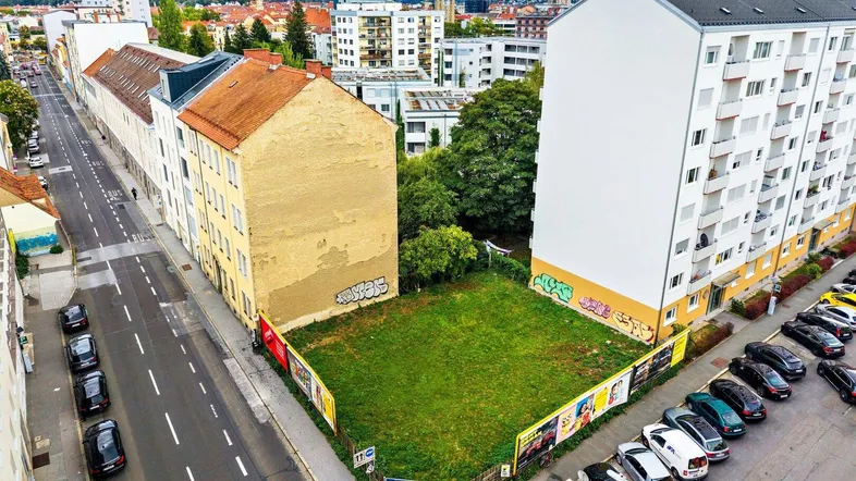 Luftaufnahme eines unbebauten Grundstücks in städtischer Umgebung, umgeben von Gebäuden und einer Straße.