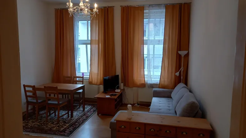 Gemütlicher Wohn-Essbereich mit Holzboden, Esstisch und Sofa, beleuchtet durch zwei Fenster.
