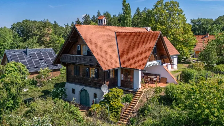Traditionelles Holzhaus mit rotem Ziegeldach, umgeben von üppiger grüner Landschaft und Bäumen.