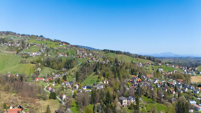 Panoramablick auf eine grüne Hügellandschaft mit verstreuten Wohnhäusern unter klarem blauem Himmel.