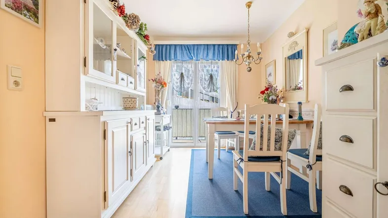 Heller Wohn- und Essbereich mit Holzboden, weißem Mobiliar und Zugang zum Balkon.