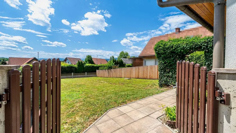Gepflegter Gartenbereich mit Rasenfläche und Holzzaun unter blauem Himmel.