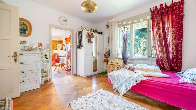 Helles Schlafzimmer mit Parkettboden, bunten Vorhängen und Blick ins Grüne.
